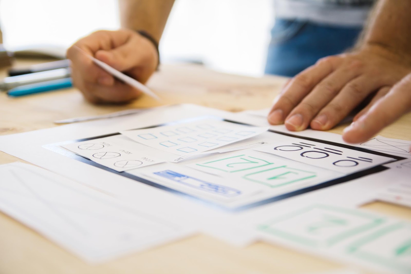 Croquis de wireframes d’interface sur des feuilles posées sur un bureau, manipulés à la main par un designer