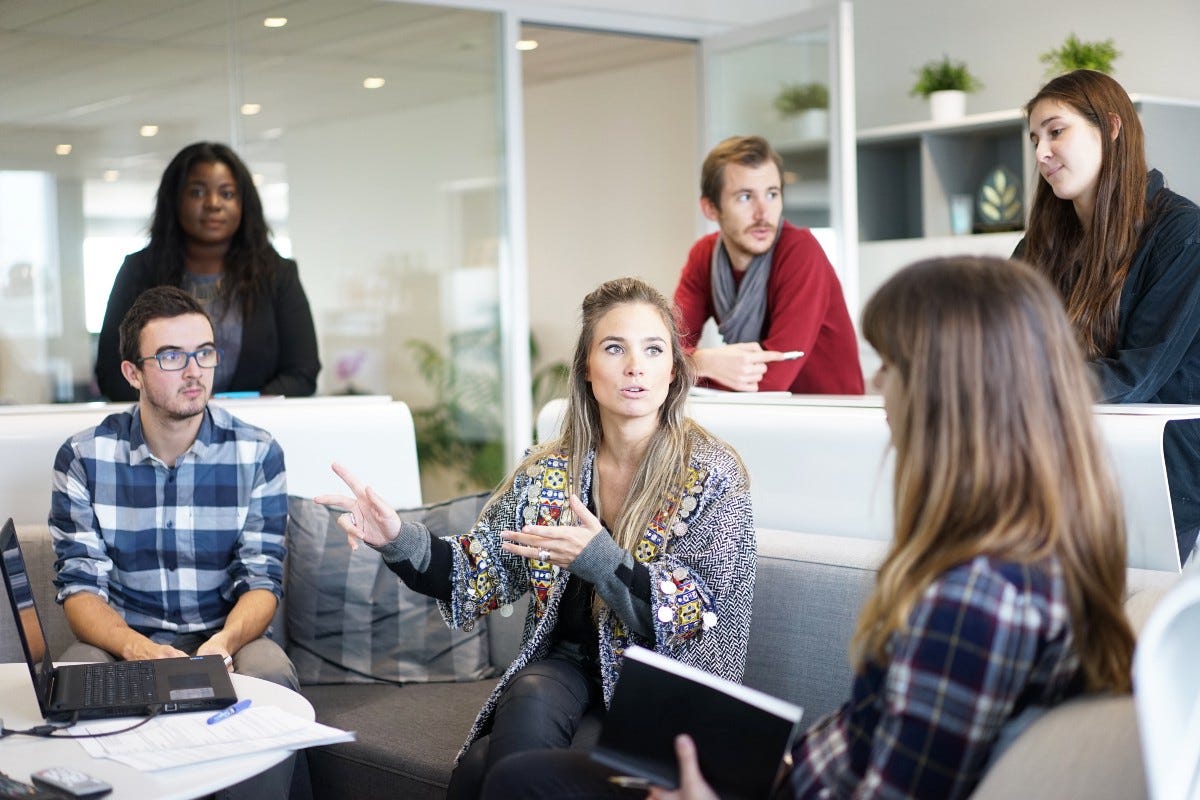 Réunion d’équipe en open space, une collaboratrice explique en gesticulant face à ses collègues assis autour d’une table basse