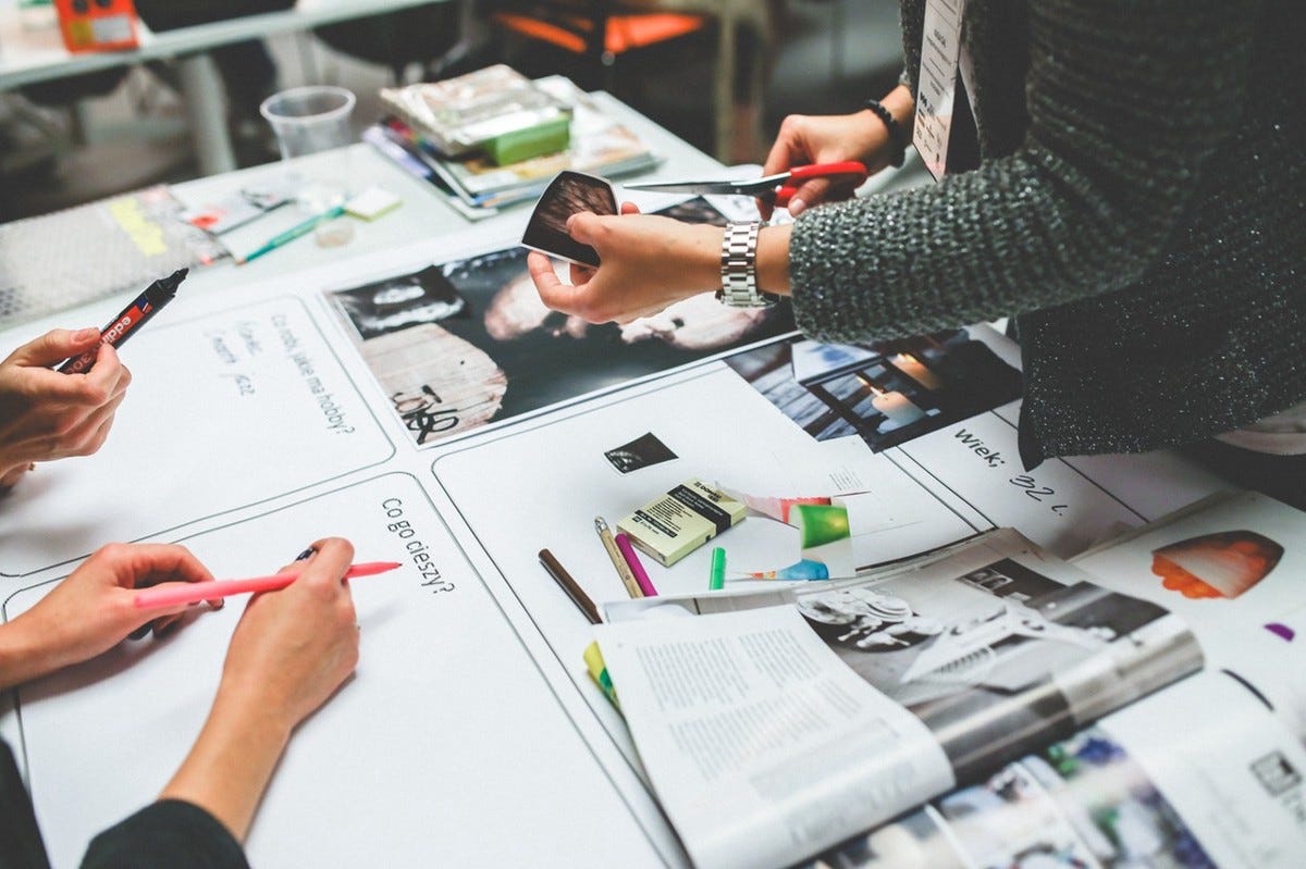 Vue de dessus d’un atelier de co-conception, des mains annotent au feutre des planches de moodboard couvertes de photos et de post-it
