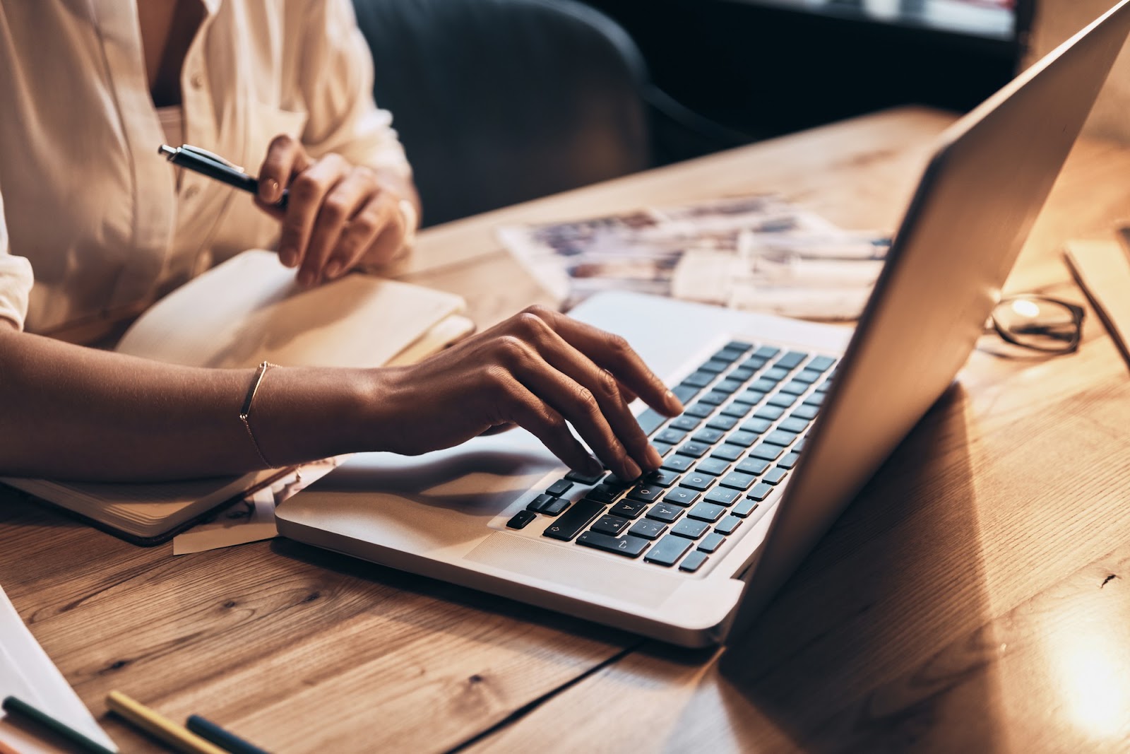 Femme travaillant sur un ordinateur portable, un stylo à la main, à une table en bois