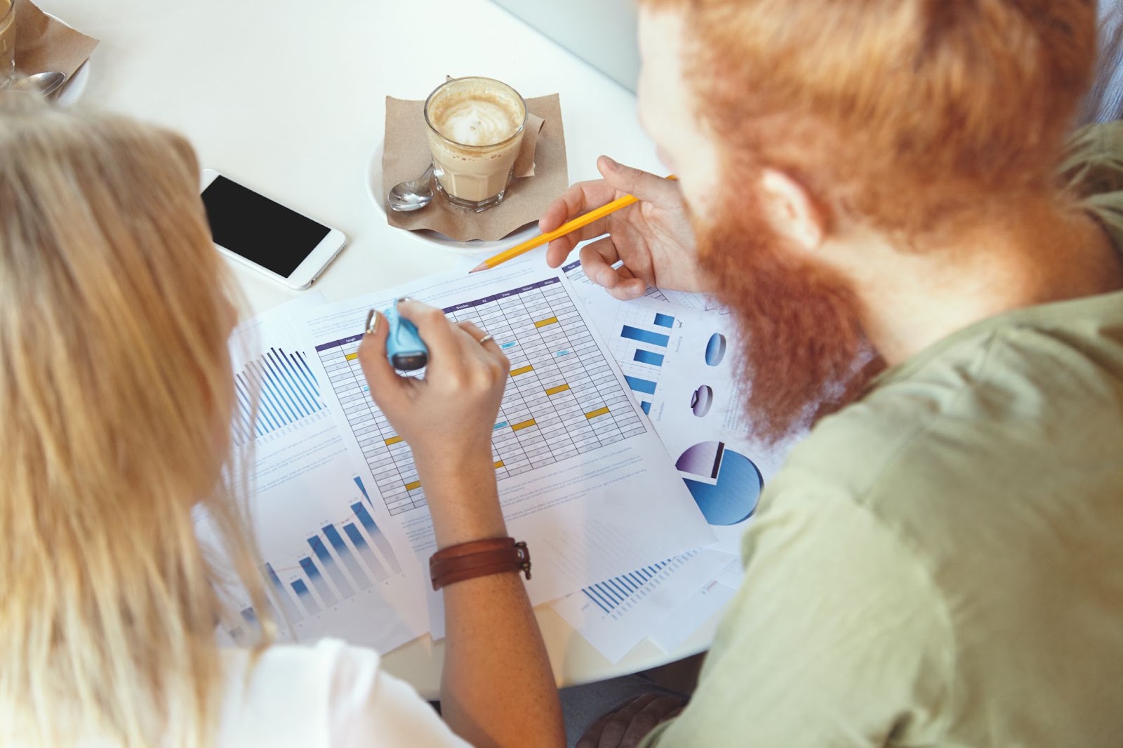 Deux collègues analysent des graphiques et tableaux imprimés autour d’un café